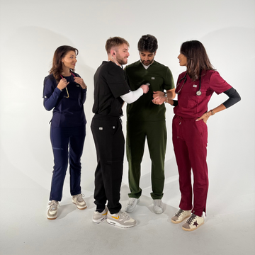 A group of doctors and nurses wearing Nila Scrubs in navy, forest green, wine red, and black, standing together in a modern clinic setting.