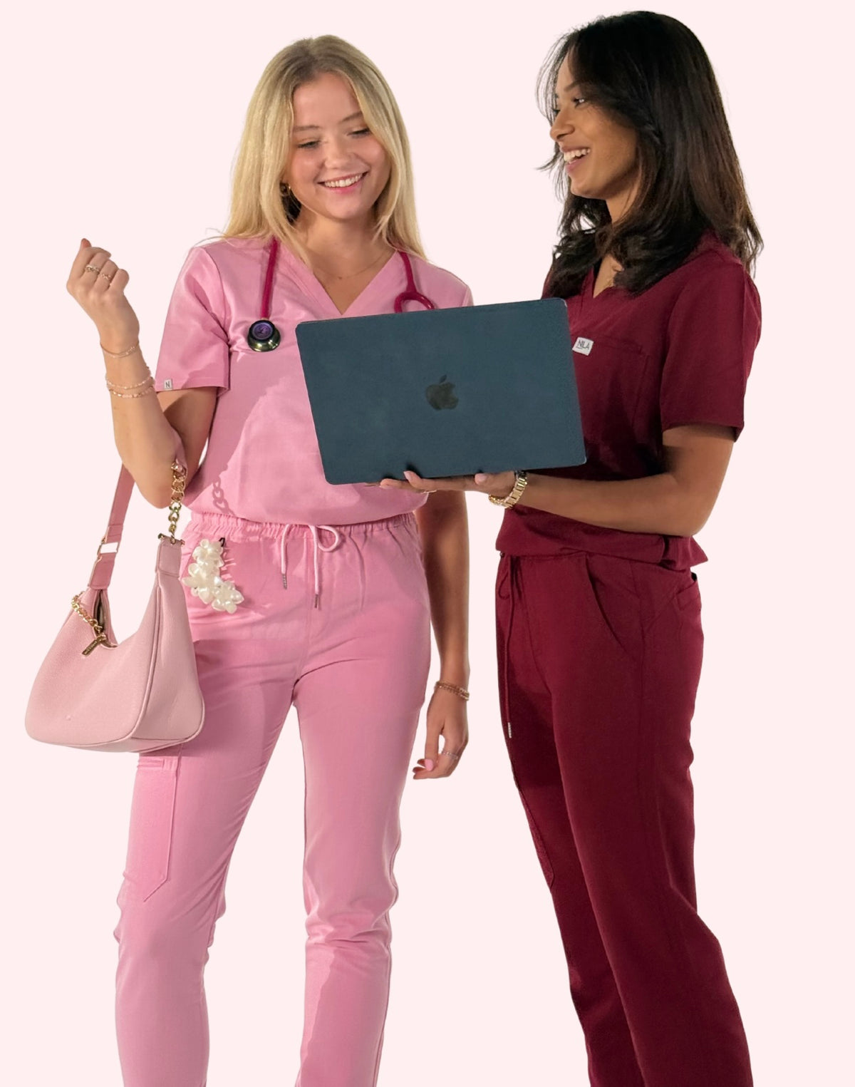 2 women wearing nila scrubs in blush pink and wine red, with stufy supplies