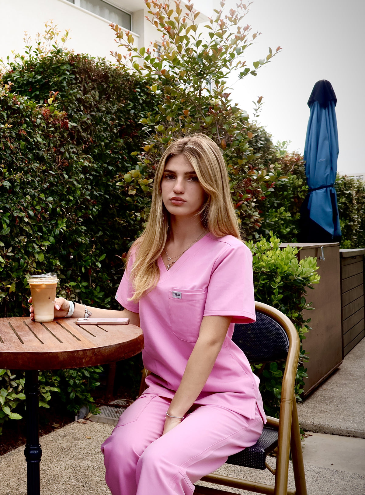 Woman sitting while wearing pink Nila scrubs in a relaxed professional setting