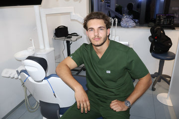 Men’s forest green Nila Scrubs medical scrub set worn seated in a dental clinic environment by a healthcare professional