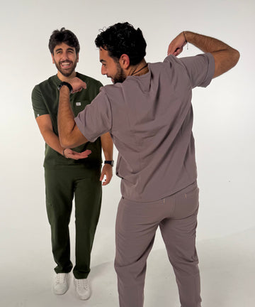 Two men wearing slate grey and forest green Nila Scrubs medical scrub sets in a clinical setting by healthcare professionals