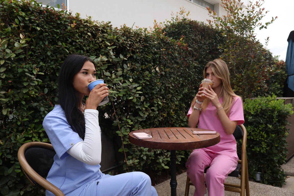 2 nurses wearing light blue nila scrubs and pink nila scrubs seated outdoors